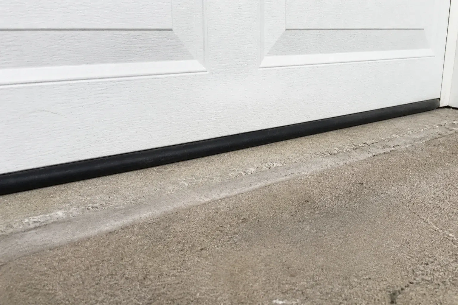 Black bottom seal along a closed white garage door at a concrete threshold. — Garage Door Bottom Seal Replacement, Barrie